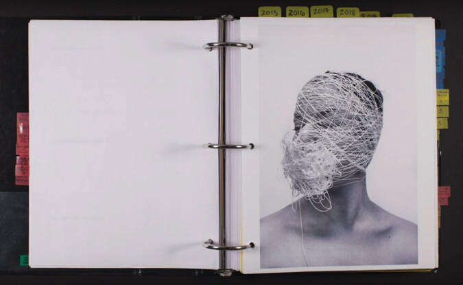 3-ring binder open to a blank page and another with photograph of figure wrapped in string